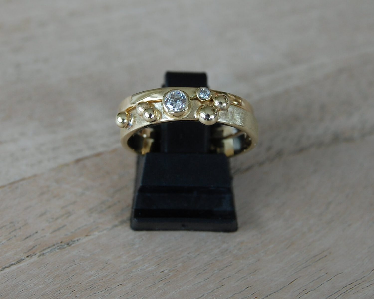 Ringen gemaakt uit aangeleverd goud - inclusief zirkonia's. In het grootste gouden bolletje op de ring is wat as opgeslagen.